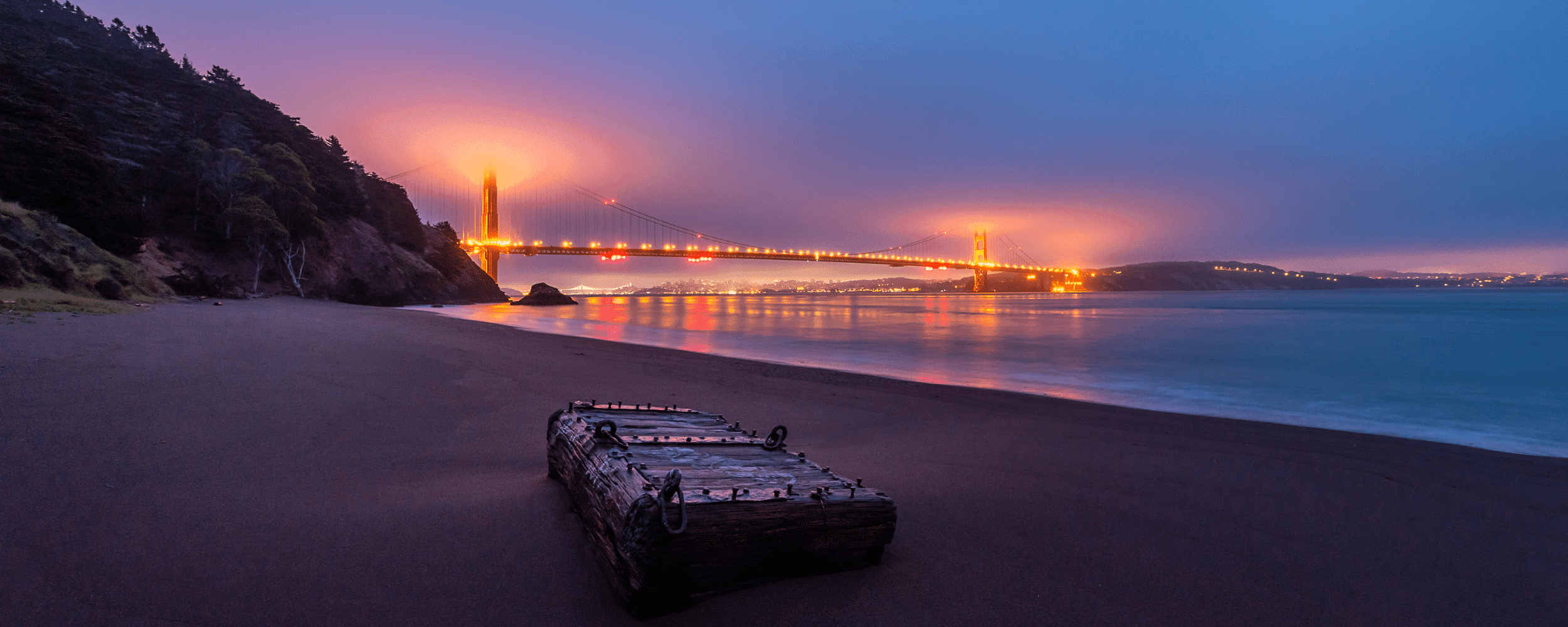 a wooden box on the banks of the kirby cove beach. the golden gate bridge all lighted up.