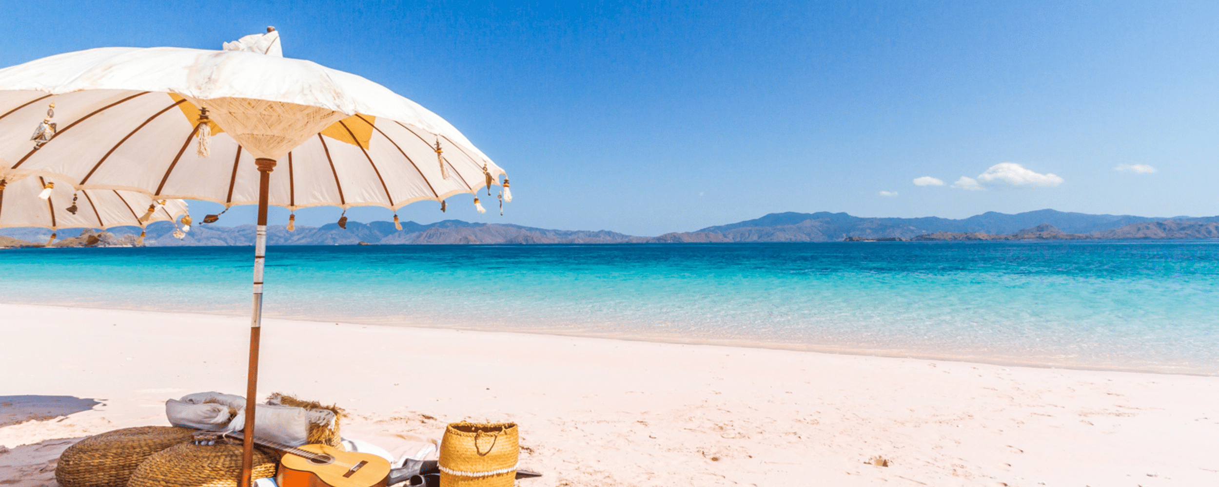 beach, pristine sand shores, a beach umbrella, picnic baskets, a guitar below the umbrella