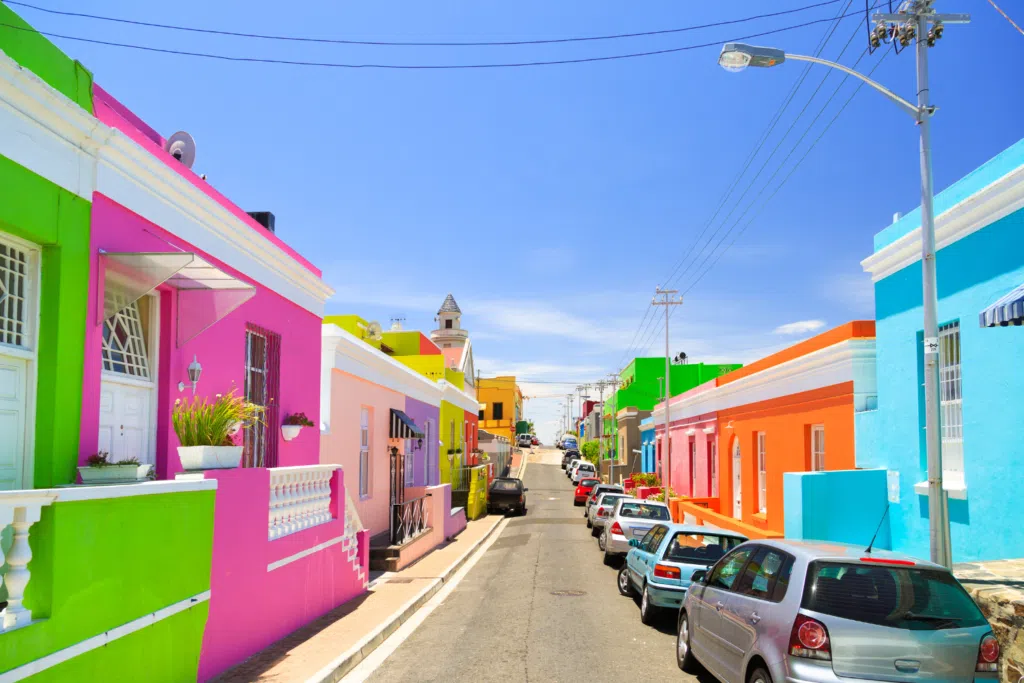 colourful street with colorful houses on either side in the Bo-kaap neighborhood. Cars parked on the sides of the road.
