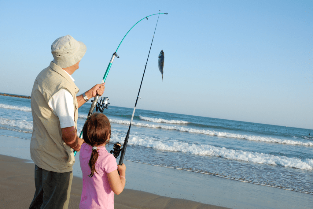 a father and daughter at the beach with two fishing rods in hand, caught one fish.
