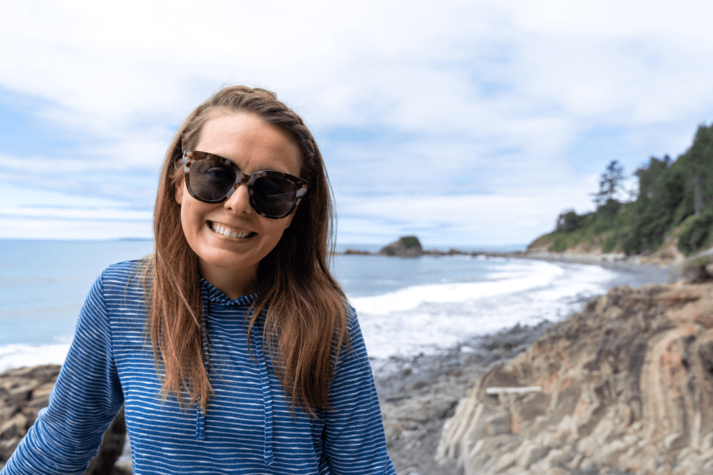 Brunette woman with long hair smiles and poses at Kalaloch Beach in Olympic National Park